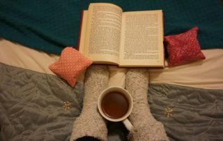 Reading book on the bed with cup of tea and bed socks