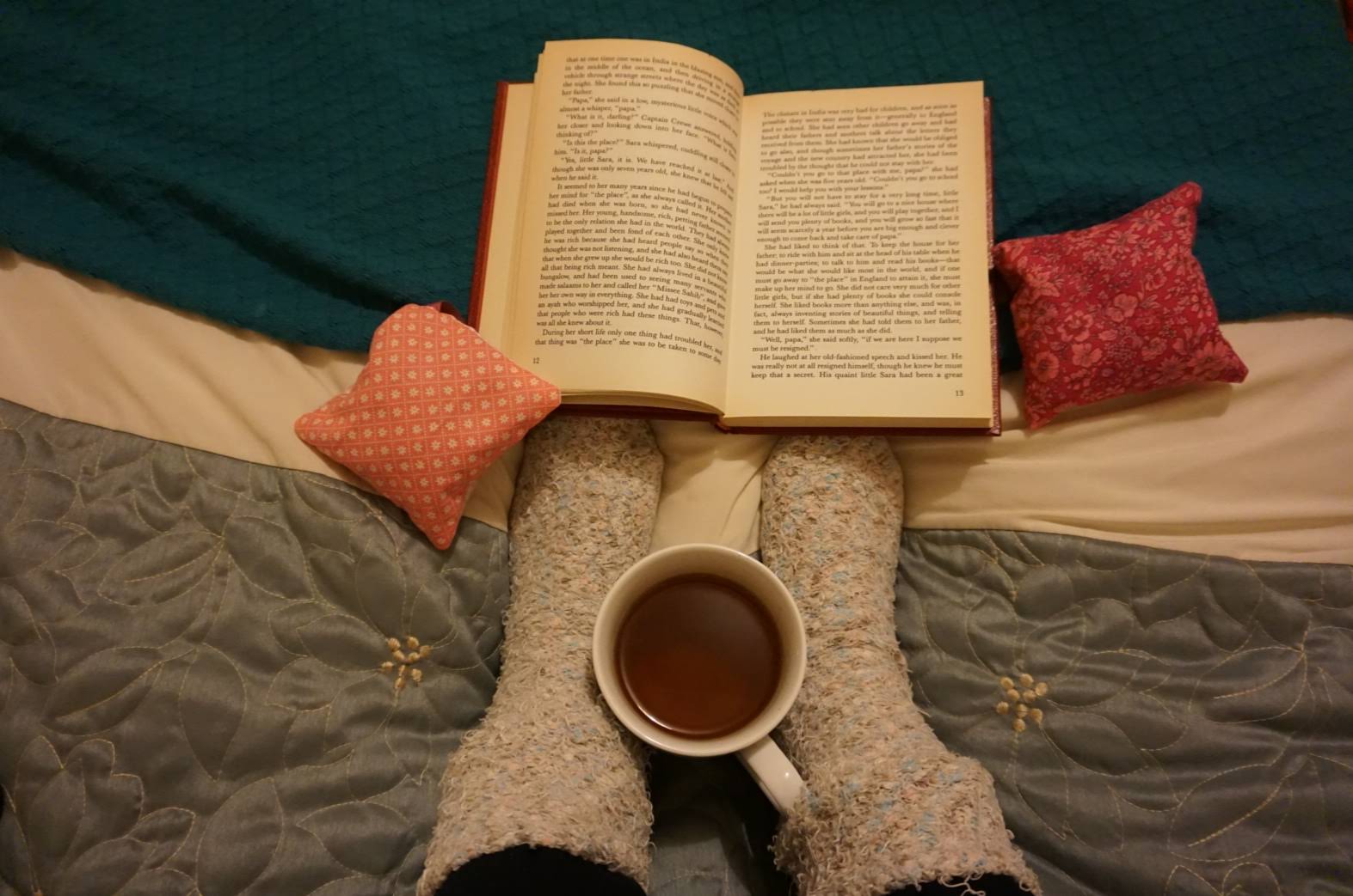 Reading book on the bed with cup of tea and bed socks